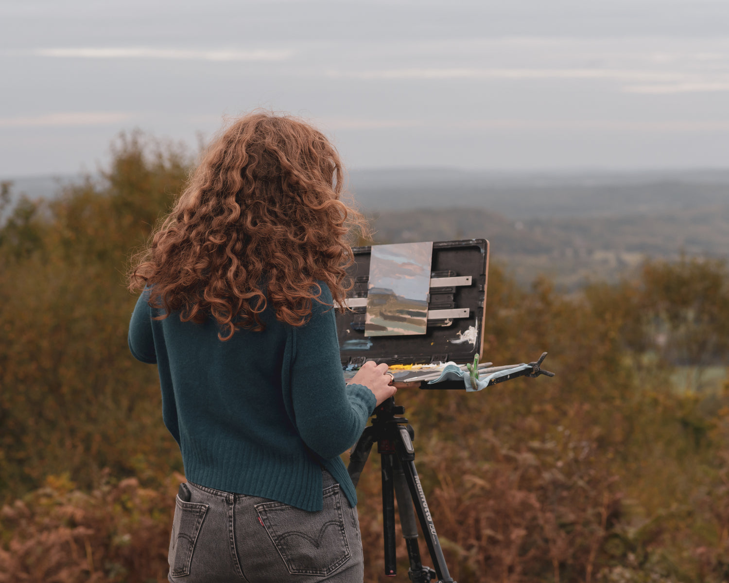 Sarah painting outdoors with a scenic landscape in the background