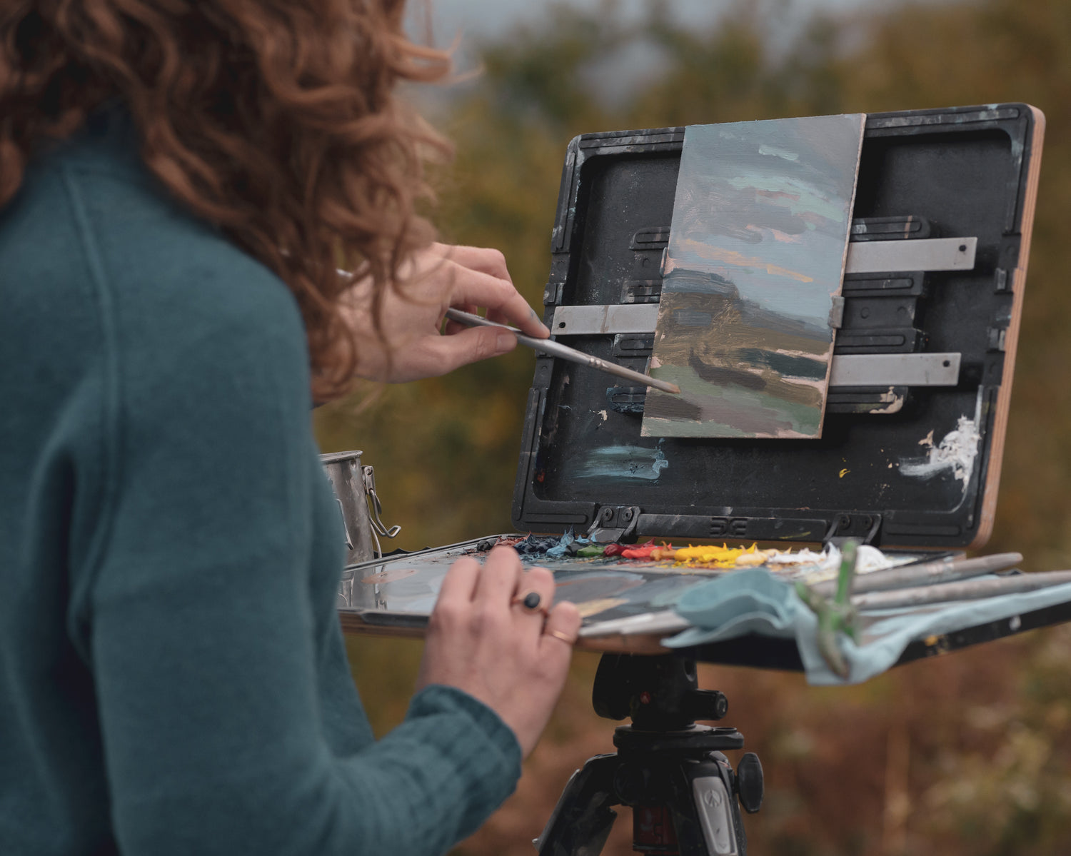 Sarah painting outdoors with a landscape scene on an easel